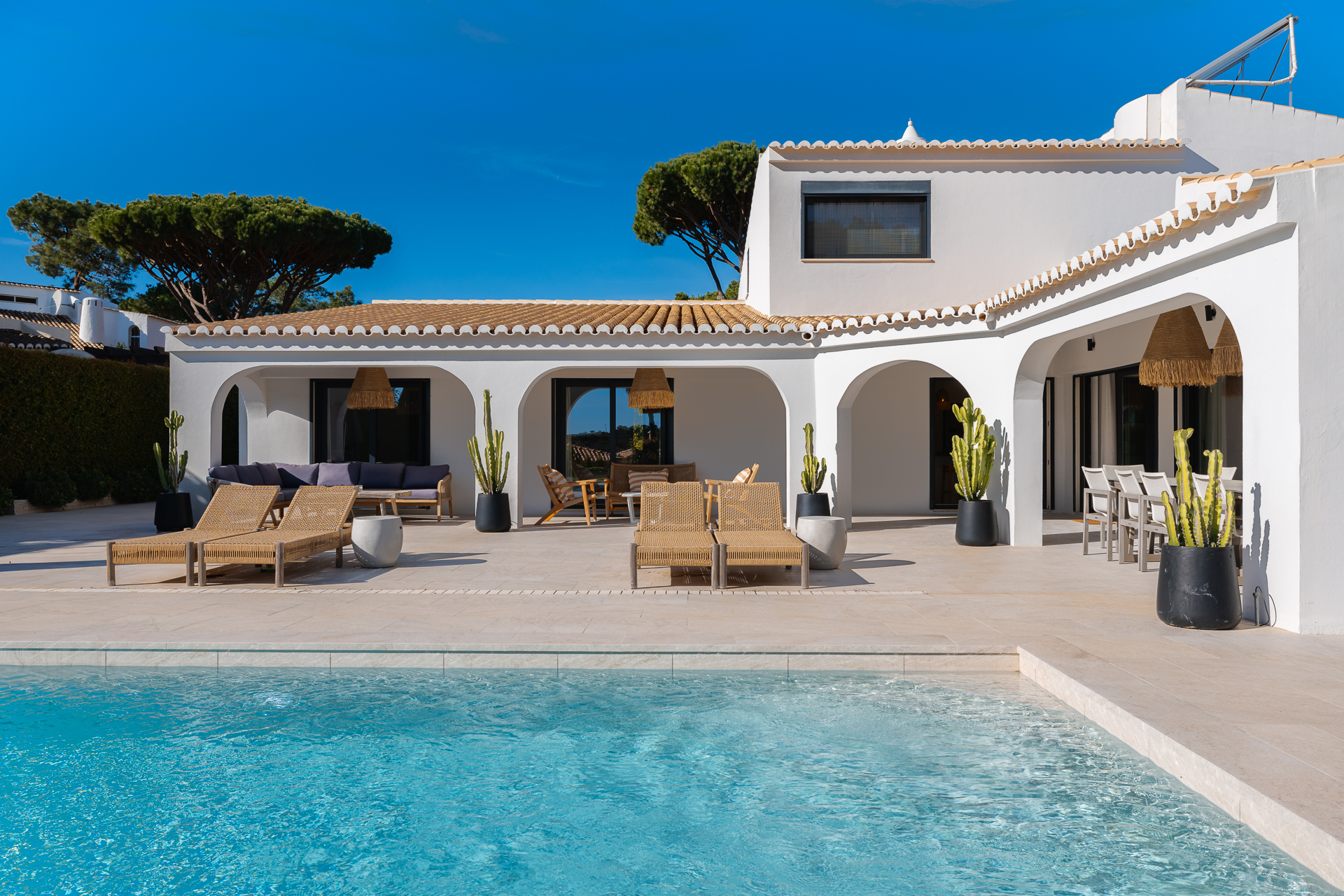 Sunlit white villa with arched terrace and a crystal clear swimming pool, styled for refined outdoor living in Portugal.